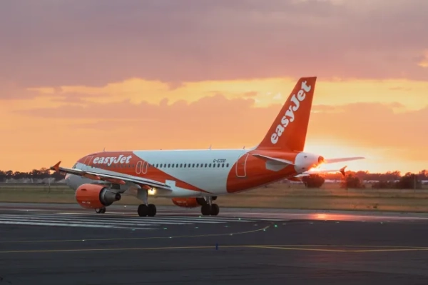 Літак Airbus A320 авіакомпанії EasyJet у помаранчево-білій лівреї на злітно-посадковій смузі аеропорту під час заходу сонця.