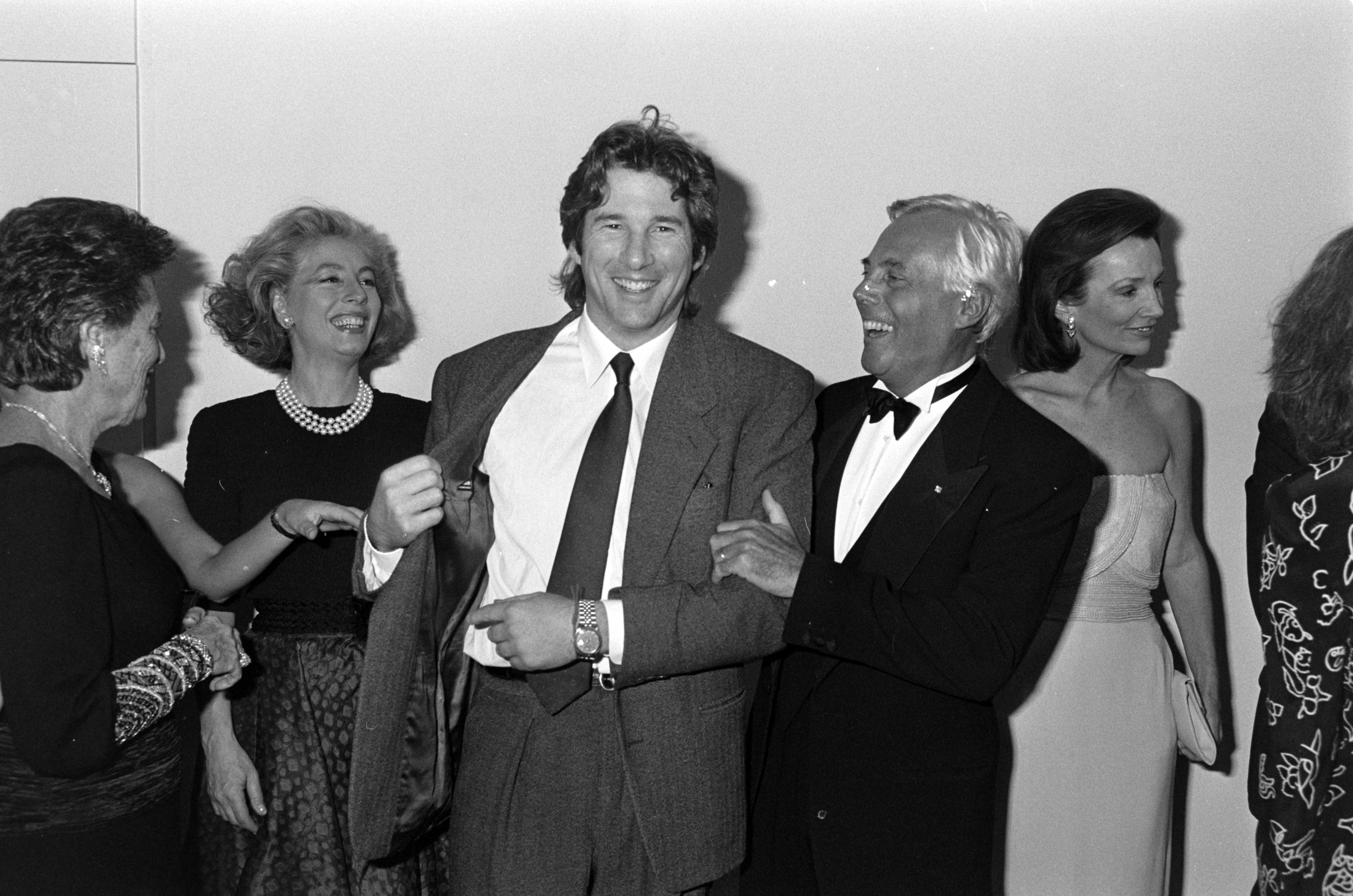 Вечеря та презентація колекції Giorgio Armani весна-літо 1988 року. Актор Річард Гір показує Giorgio Armani етикетку на своєму костюмі, а гості та світська левиця Лі Радзівілл спостерігають.4