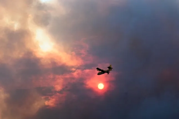 На цій фотографії зображено літак Canadairs CL-415 (31/F-ZBFP) французької цивільної безпеки, що летить, коли сонце ховається за густим димом під час лісової пожежі поблизу Фонжонкуза, на південному заході Франції, 6 серпня 2025 року. Лісова пожежа забрала життя однієї людини та поранила дев'ятьох інших, охопивши 11 000 гектарів, поки пожежники працюють над її стримуванням, повідомили місцеві чиновники. Пожежа, яка почалася напередодні, знищила або пошкодила 25 будинків у південному департаменті Од, де понад 1800 пожежників боролися за контроль над тим, що зараз є найбільшою лісовою пожежею у Франції цього літа. (Фото Ліонеля Бонавентюра / AFP) (Фото Ліонеля Бонавентюра/AFP через Getty Images)