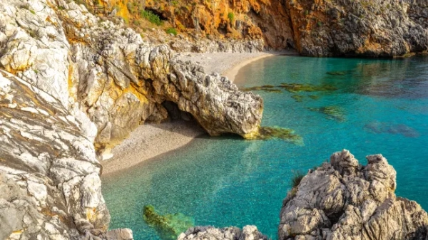 Порожній пляж з бірюзовим морем, оточений скелями, під назвою Кала-Капрерія в природному заповіднику Різерва-делло-Цінгаро на Сицилії, Італія.