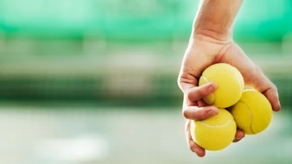 Рука, що тримає три тенісні м'ячі.