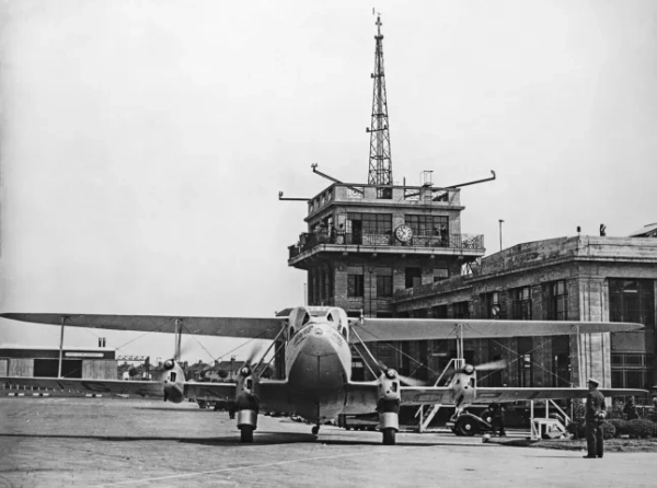 2FNCRJ1 Вінтажна чорно-біла фотографія літака Imperial Airways De Havilland DH.86 Express з реєстрацією G-ACPL та назвою «Delphinus» в аеропорту Кройдон, Лондон, 1930-ті роки. Диспетчерська вежа аеропорту позаду.