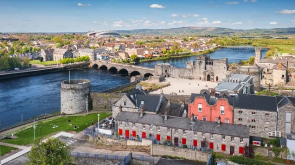 Вид з повітря на місто Лімерик у сонячний день в Ірландії, на якому видно міст через річку, різні будівлі та пагорби вдалині.