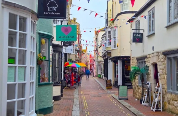 Вид на головну вулицю Сент-Олбан у Веймуті, графство Дорсет, з низкою незалежних магазинів та вивісок кав'ярень над дверними отворами, а також вивісками вздовж вулиці.