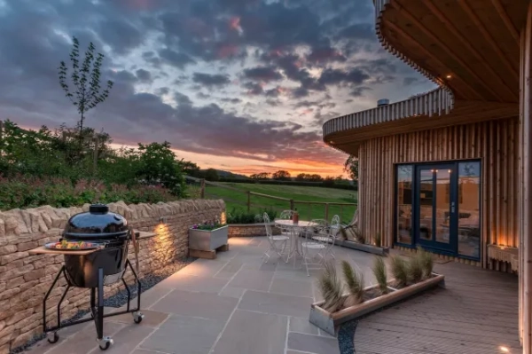 Тераса біля лоджу з барбекю Weber та столом на чотирьох осіб на заході сонця.