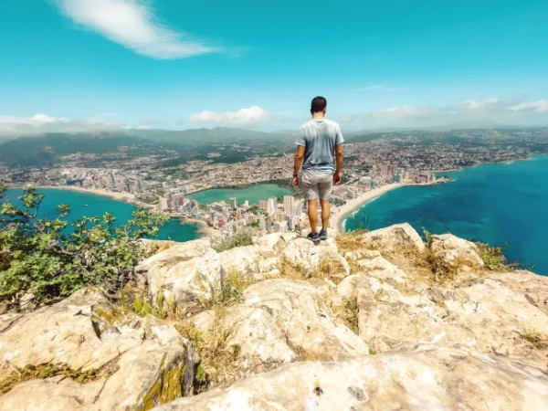 Чоловік стоїть на вершині гори Іфак з видом на океан та Аліканте внизу.