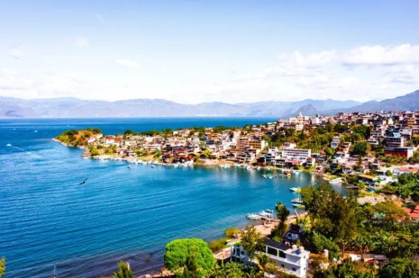 Приголомшливий краєвид на узбережжя Гватемали, з яскраво-блакитним морем, над яким видніються будинки та зелень, та горами вдалині.