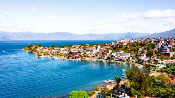 Приголомшливий краєвид на узбережжя Гватемали, з яскраво-блакитним морем, над яким видніються будинки та зелень, та горами вдалині.