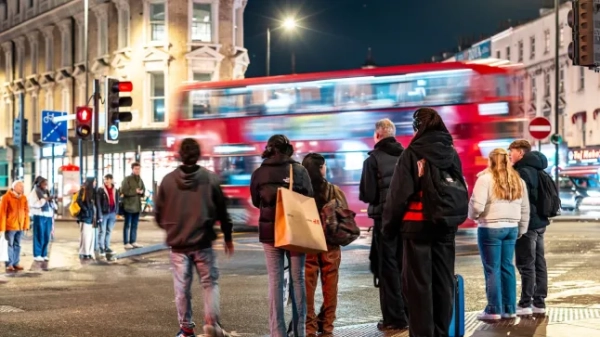 Туристи чекають на перехресті вночі в Лондоні, поки повз проноситься червоний двоповерховий автобус.