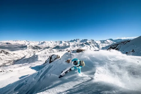 Лижник стрибає через схил, за яким стоять кілометри трас на курорті Ле-Сібель у Французьких Альпах.