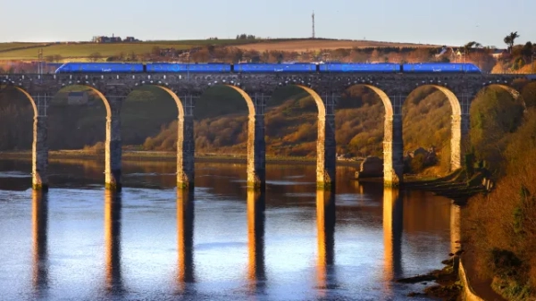 Вид на синій поїзд Lumo, що їде над річкою по високому арочному мосту.