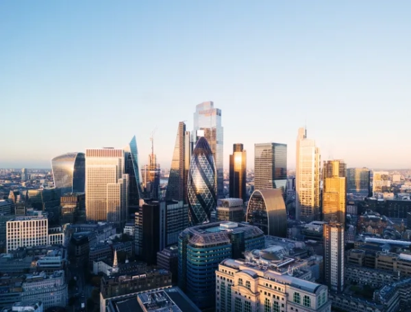 Вид з висоти пташиного польоту на лондонське Сіті на заході сонця. Багато висотних будівель відбивають сонце, а за ними — світло-блакитне небо. На небі немає жодної хмаринки.