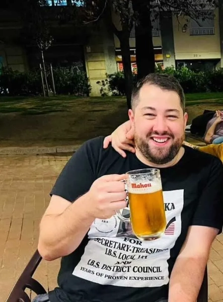 Росс Маккаферті посміхається в чорній футболці та тримає пінту пива в руках.