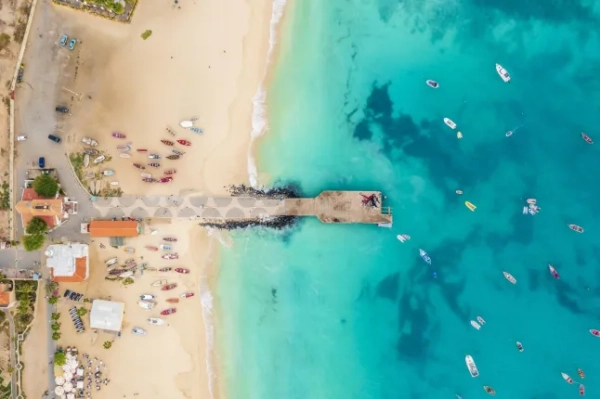 Вид з повітря на бірюзове море та золотий піщаний пляж Кабо-Верде з човнами, розкиданими вздовж води та берега.