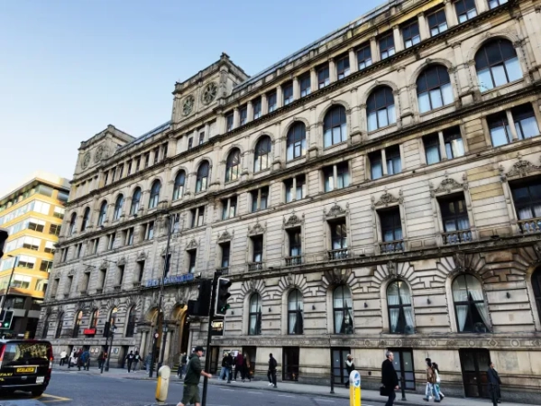 Історична кам'яна будівля готелю Britannia вздовж жвавої вулиці Манчестера з пішоходами та арочними вікнами