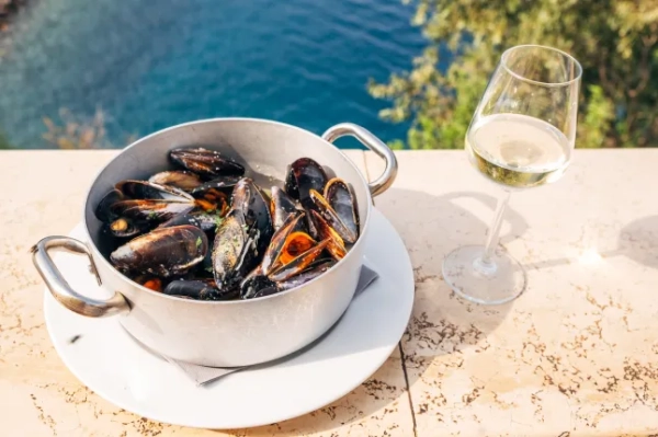 каструля з мідіями та келих вина на тлі моря
