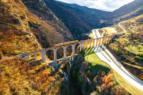 Вид з повітря на жовтий поїзд, що перетинає арочний міст у мальовничій осінній сільській місцевості Франції.