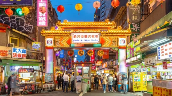 Вхід до нічного ринку на вулиці Раохе – одного з найстаріших нічних ринків у Тайбеї, Тайвань – з барвистою аркою, ліхтарями, що висять над нею, та освітленими кіосками з обох боків.