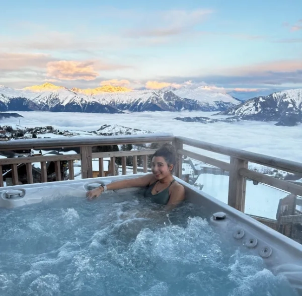 Зінеб у джакузі з видом на Французькі Альпи. На ній темно-сірий купальник.