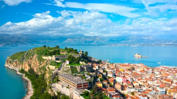 Вид з повітря на старе місто Нафпліон на грецькому Пелопоннесі, на якому видно півострів і будинки з помаранчевими дахами, оточені блакитним морем, у яскравий сонячний день.